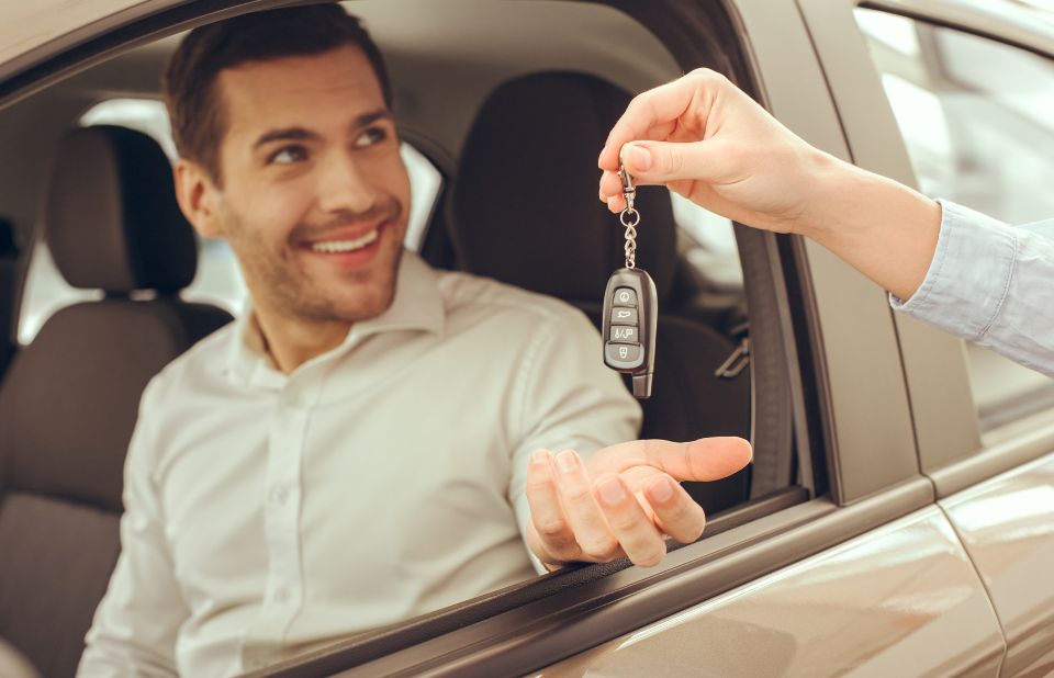 Handing over car keys to person sitting inside a vehicle.