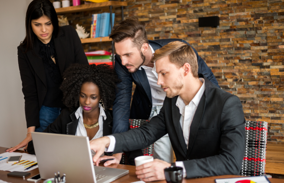 Group of professionals discussing over a laptop in a meeting room with brick wall background.