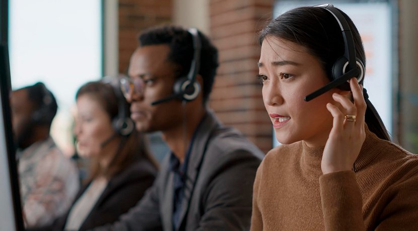 Three people wearing headphones in a row, one touching an earpiece, in an office setting.