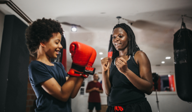 Two individuals in a gym practicing boxing with one wearing red gloves.
