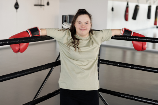 Person with red boxing gloves leaning on the ropes of a boxing ring.