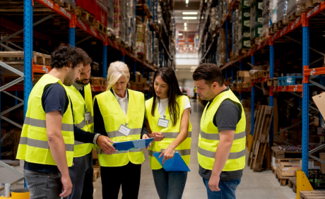 Workers in high-visibility vests discussing over documents in a warehouse.